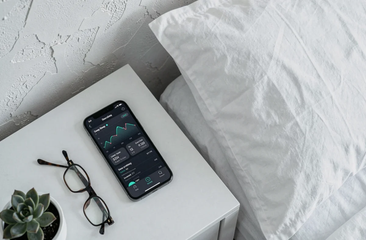 Smartphone affichant une application de suivi du sommeil avec graphiques des cycles et du sommeil profond, posé sur une table de nuit